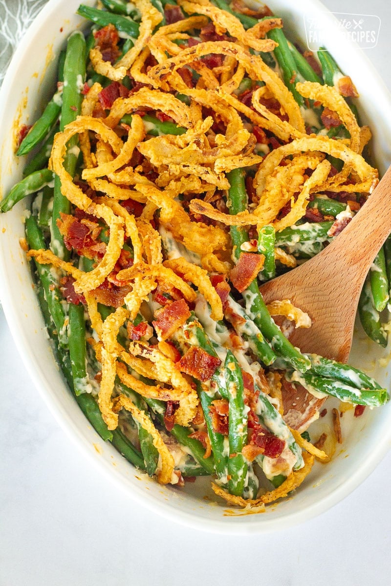 This Green Bean Casserole is made with fresh green beans and a homemade creamy sauce. No cream-of soups or canned onions in this dish! Dish of Green Bean Casserole with a wooden spoon.