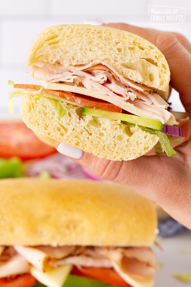 Hand holding sliced in half Subway Bread sandwich.