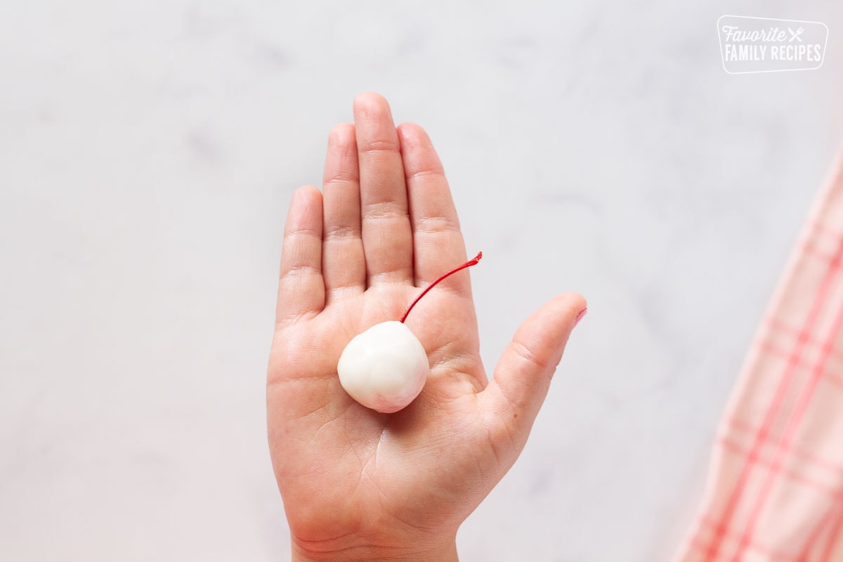 Hand holding a single cherry covered in fondant for Chocolate Covered Cherries.