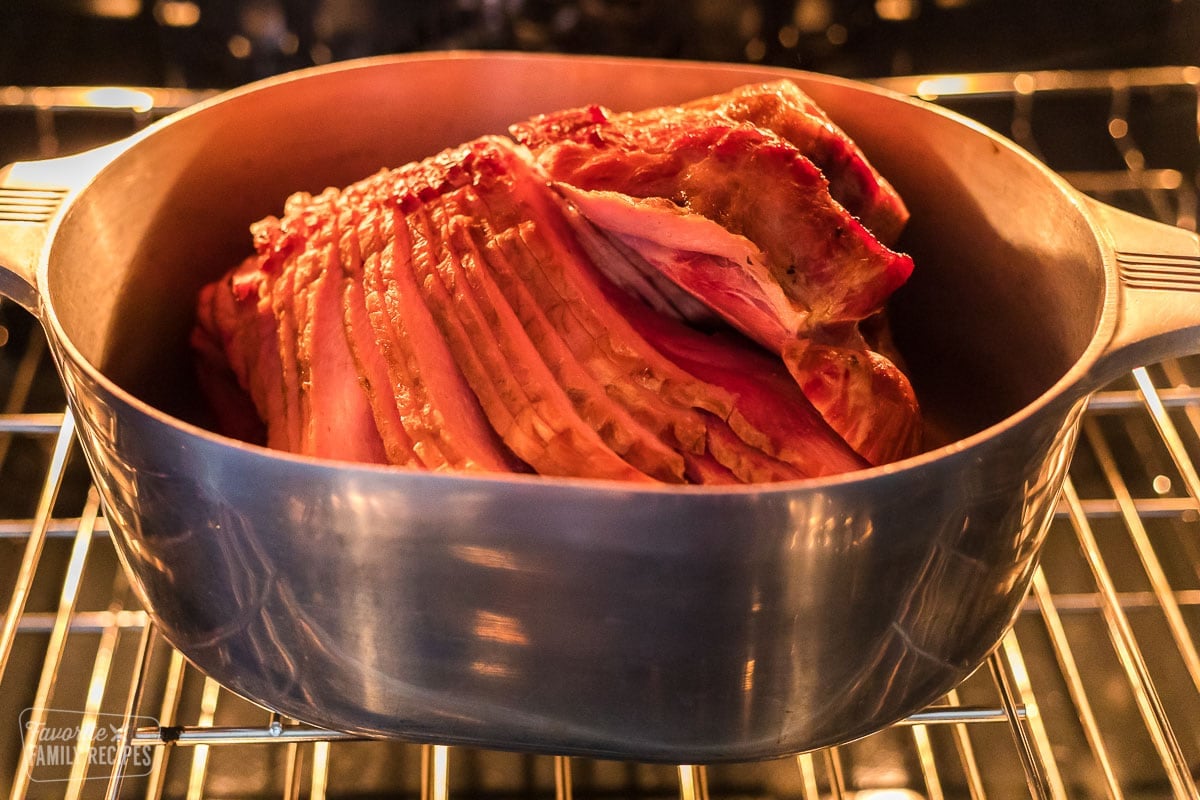 Honey baked ham being cooked in a roasting pan in the oven