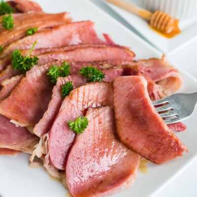 Slices of honey baked ham on a plate with a fork