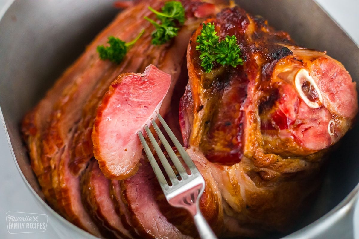 A honey baked ham in a roasting pan with a honey glaze