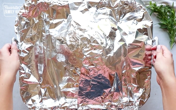 A roasting pan with a ham covered in foil