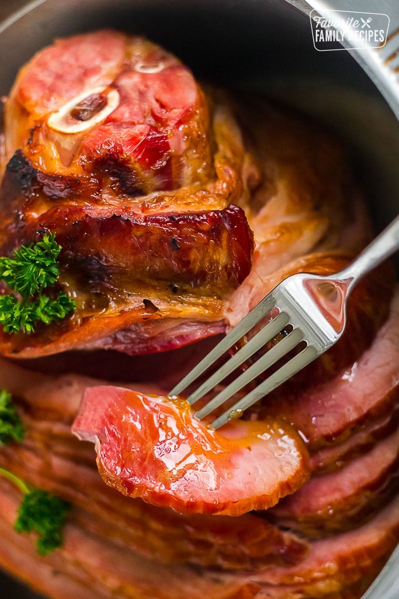 A honey baked ham in a roasting pan showing the honey glaze