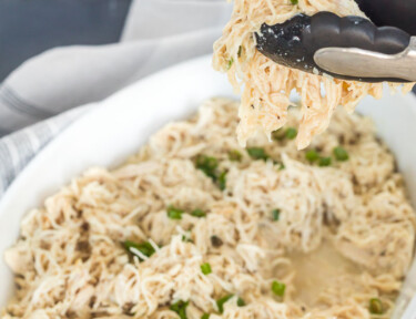 Instant pot shredded chicken being lifted from a serving dish with tongs