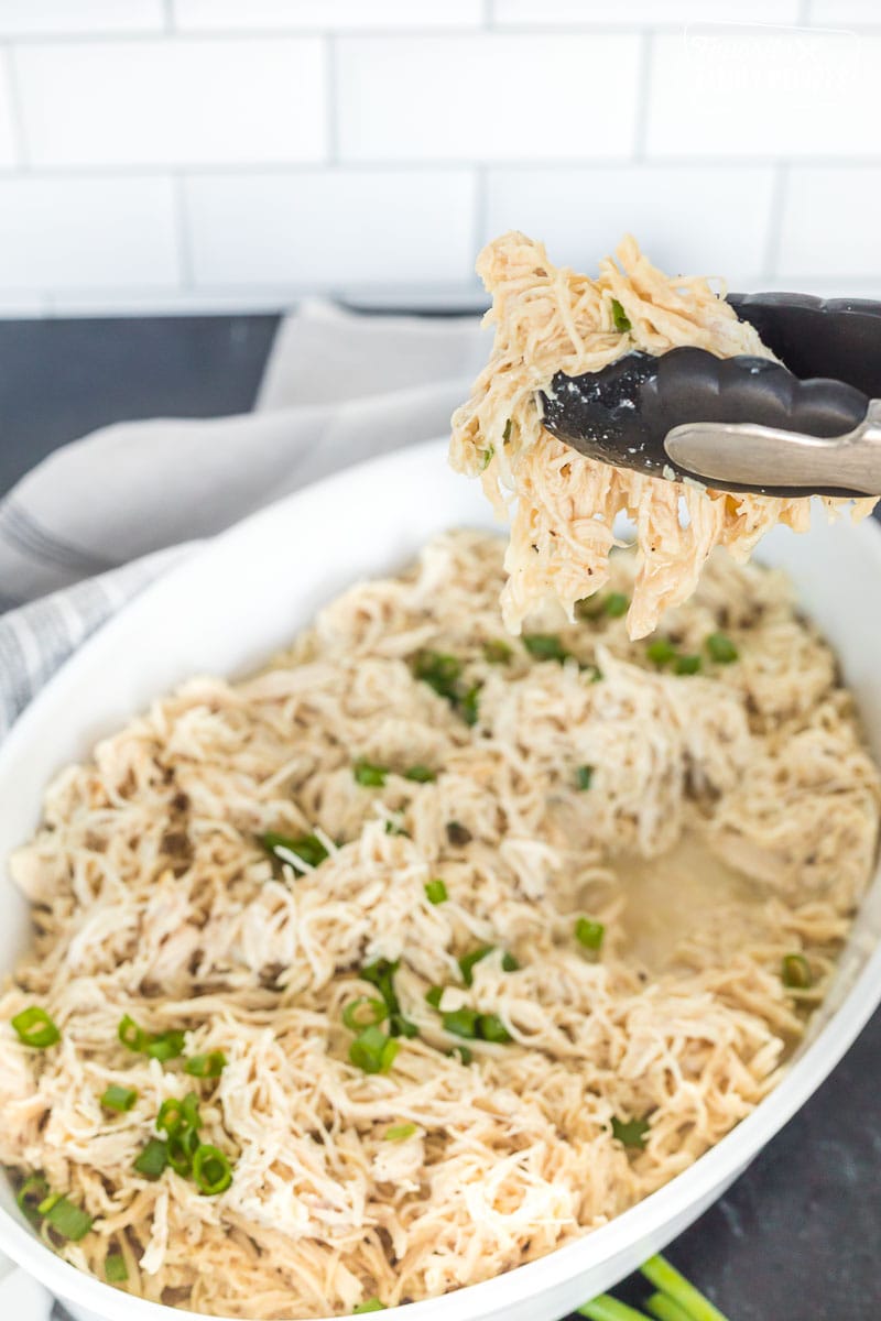 Instant pot shredded chicken being lifted from a serving dish with tongs.