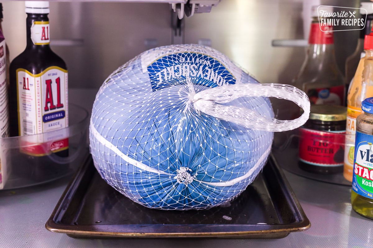 A large frozen turkey on a tray in the fridge thawing