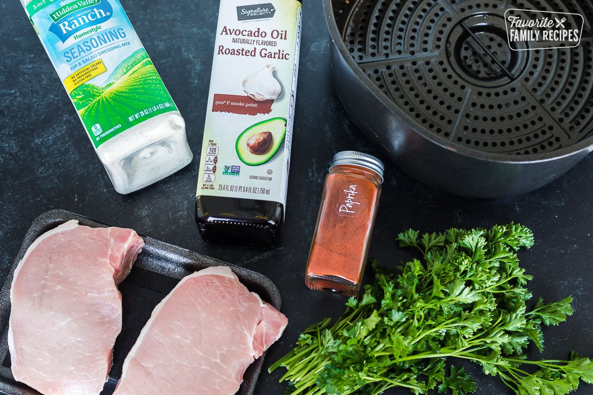 Ingredients to make air fryer pork chops including paprika, ranch seasoning, oil, and parsley.