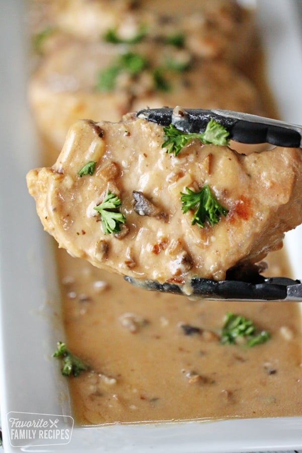 Tongs holding a pork chop that was cooked in the instant pot.