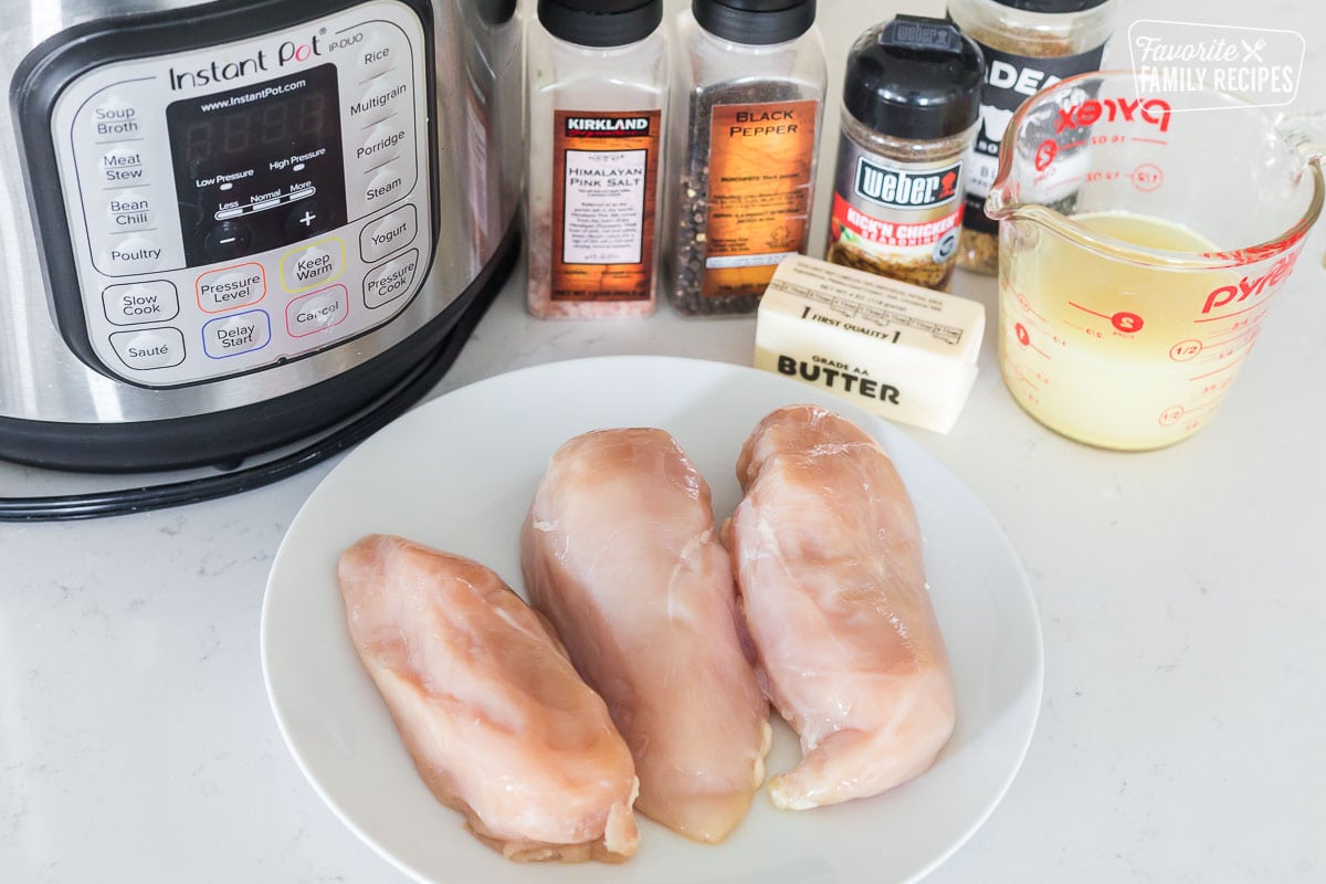 Three pieces of chicken on a plate next to ingredients to make Instant Pot shredded chicken.