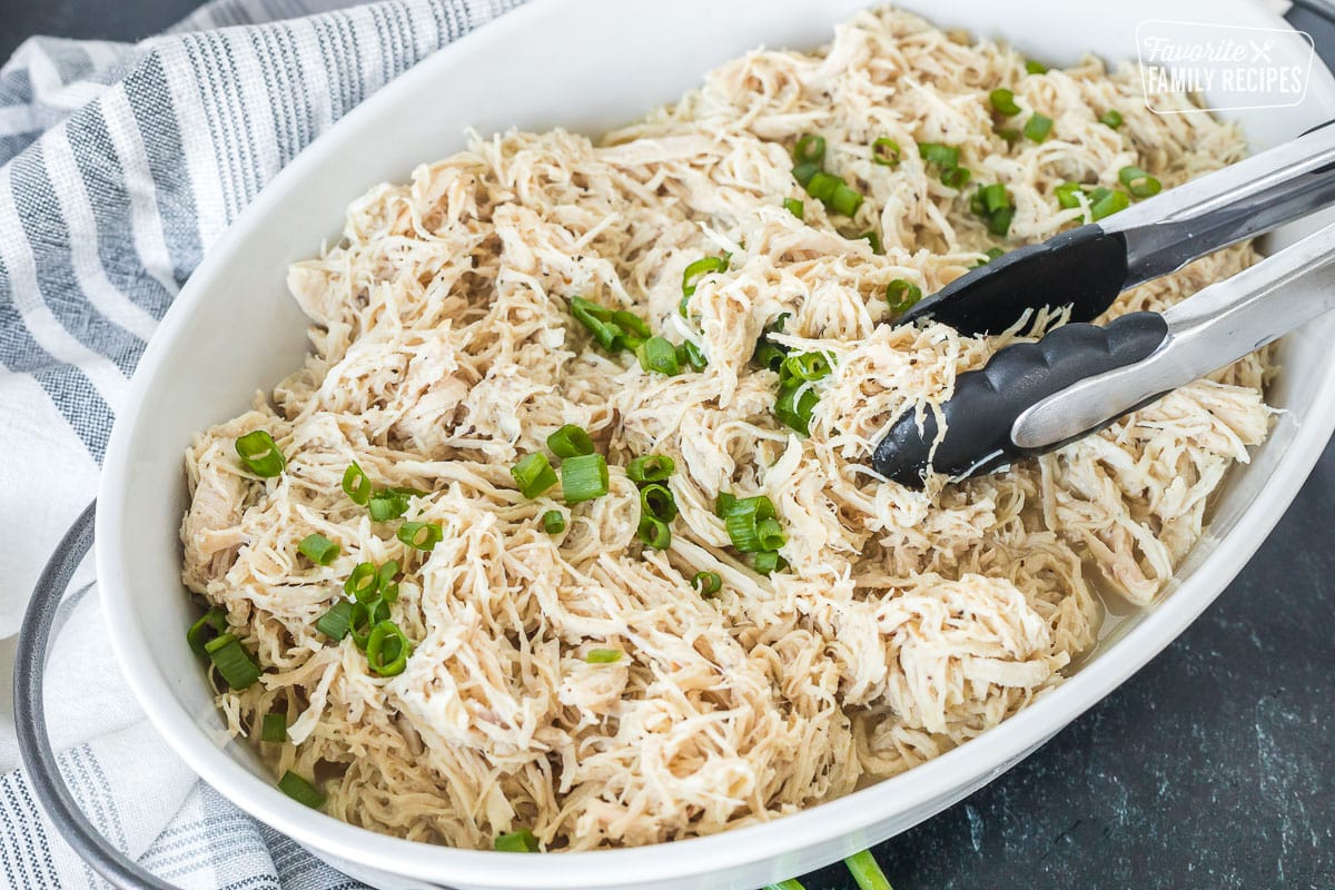 A dish with shredded chicken and tongs.