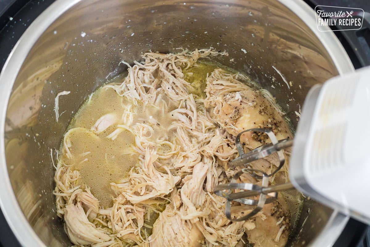 A hand mixer shredding chicken in an Instant Pot.