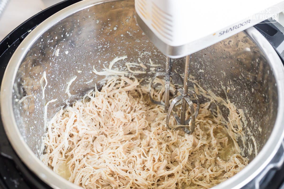 Chicken being finely shredded with a hand mixer