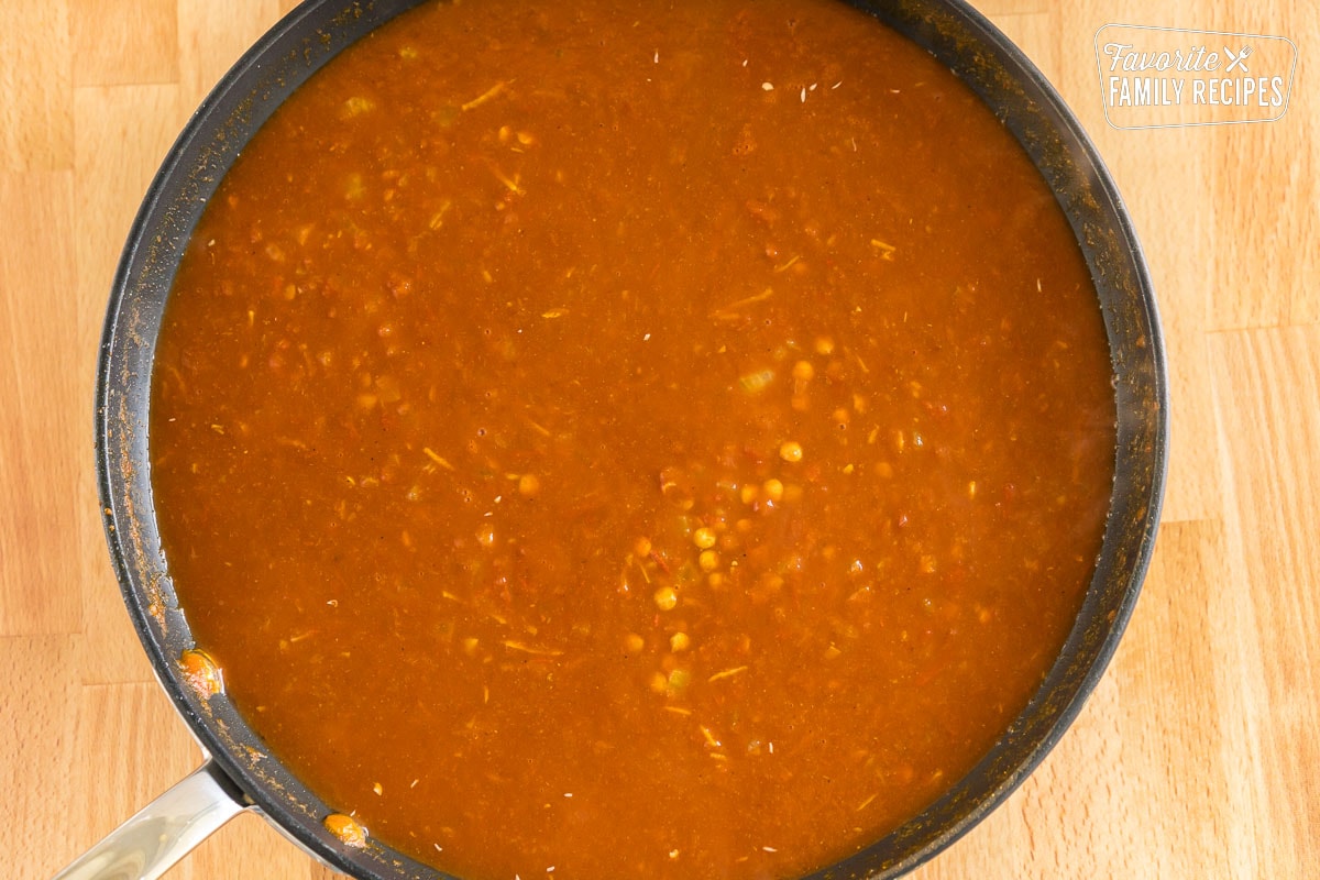 A large skillet with lentils, tomatoes, broth, and spices