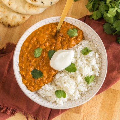 Lentil curry in a bowl with rice topped with cilantro and plain yogurt