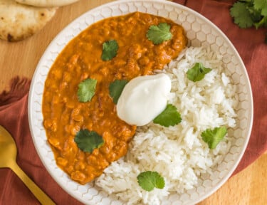 Lentil curry in a bowl with rice topped with cilantro and plain yogurt