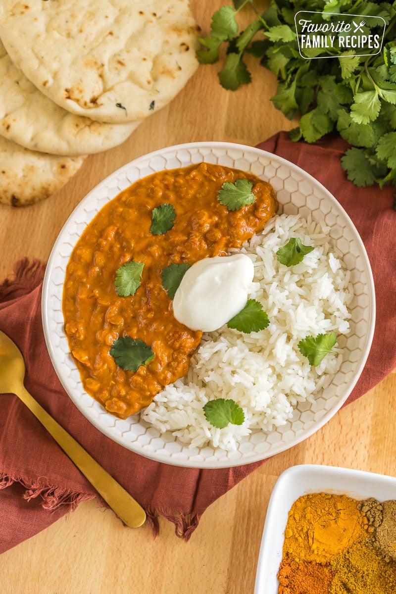 Vegan lentil curry in a bowl with rice topped with cilantro and plain yogurt.