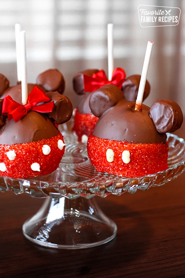 Mickey and Minnie caramel apples on a glass cake stand.