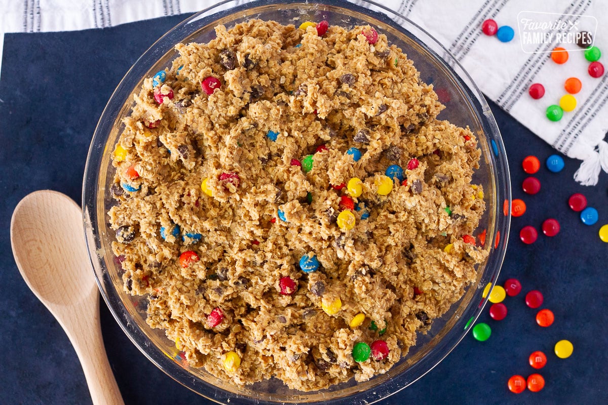 Bowl of Monster Cookie dough with a wooden spoon and M&Ms on the side.