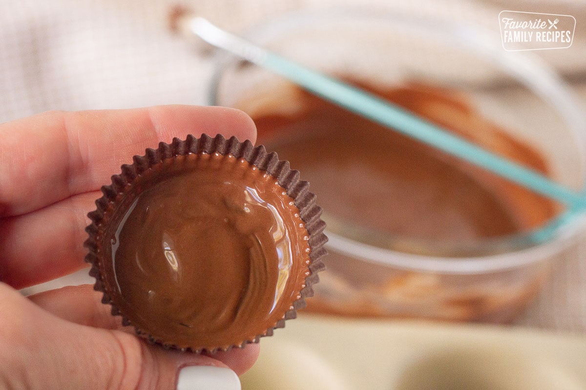 Hand holding a painted liner for the bottom layer of Homemade Reese's Peanut Butter Cups.