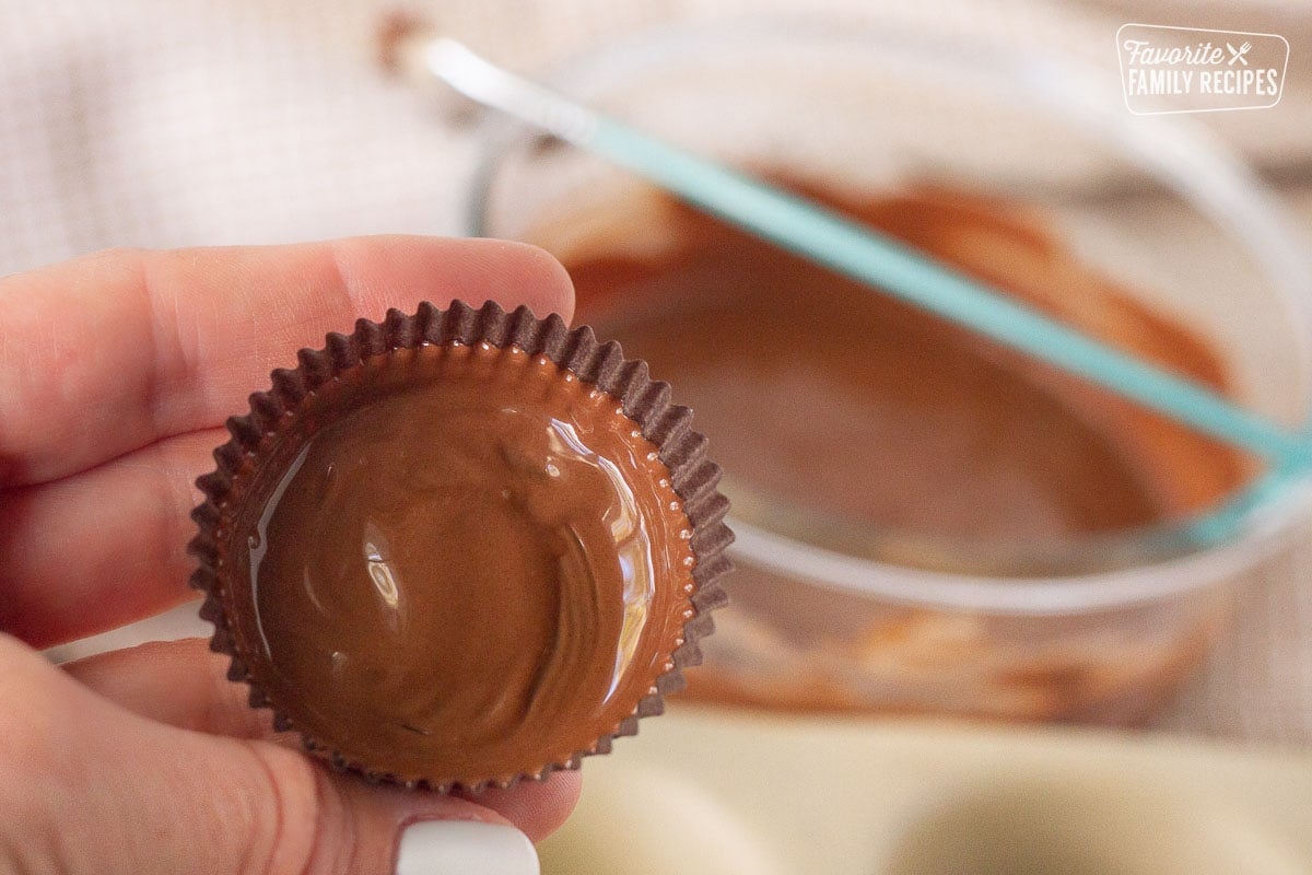 Hand holding a painted liner for the bottom layer of Homemade Reese's Peanut Butter Cups.