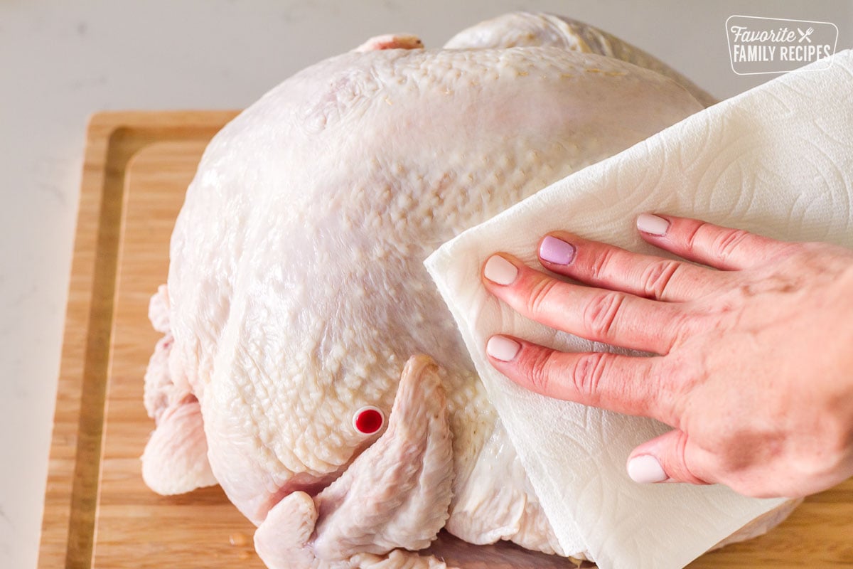Hand patting turkey dry with paper towels for How to Cook a Turkey Instructions.
