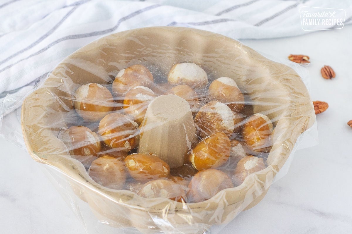 Bundt pan with unbaked Easy Monkey Bread topped with plastic wrap.