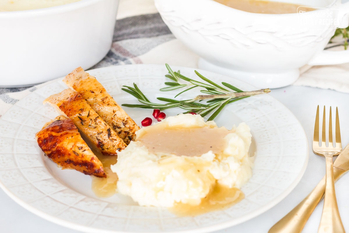 Plate of turkey and mashed potatoes topped with Turkey Gravy. Fresh rosemary for garnish.