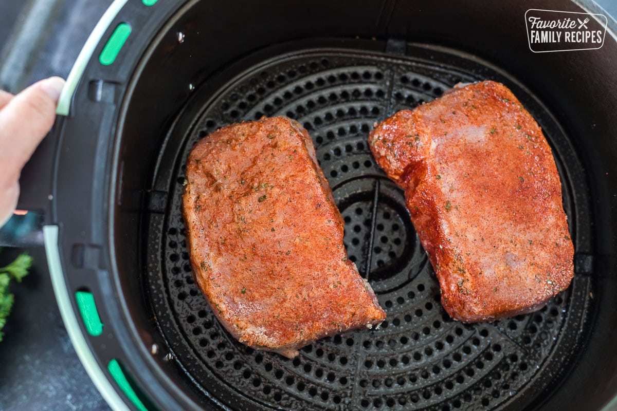 Two seasoned and raw pork chops in an air fryer basket