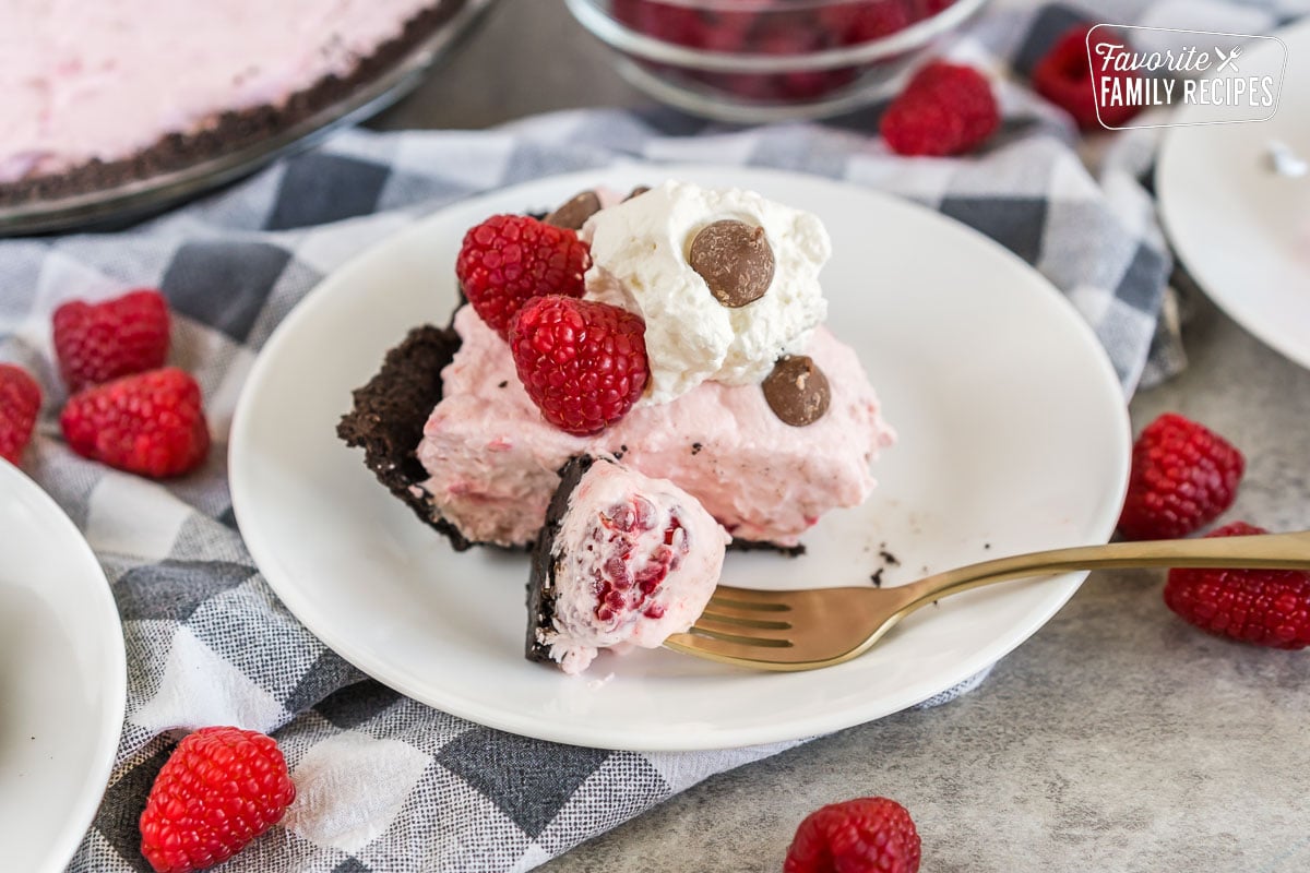 A slice of Raspberry Cream Pie on a plate topped with raspberries, whipped cream, and chocolate chips