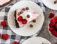 Three slices of Raspberry Cream Pie on plates topped with whipped cream, raspberries, and chocolate chips