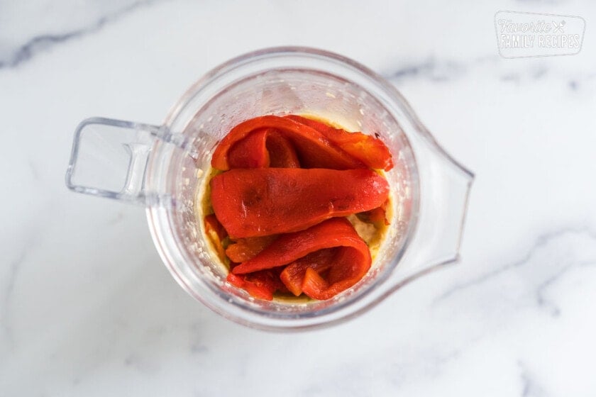 A blender with chickpeas, roasted red peppers, garlic, olive oil, lemon, salt and pepper