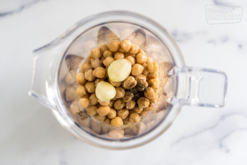 A blender full of chickpeas, garlic, salt and pepper