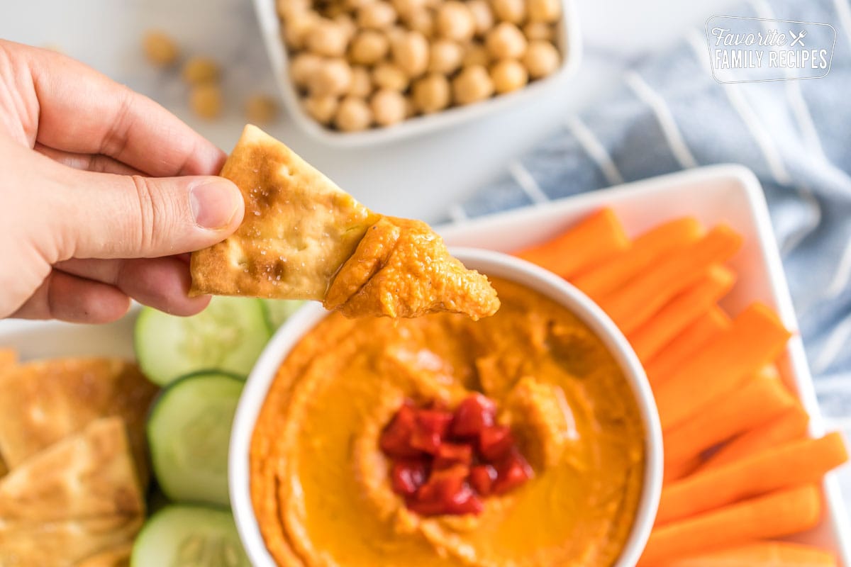 A pita chip dipped in roasted red pepper hummus