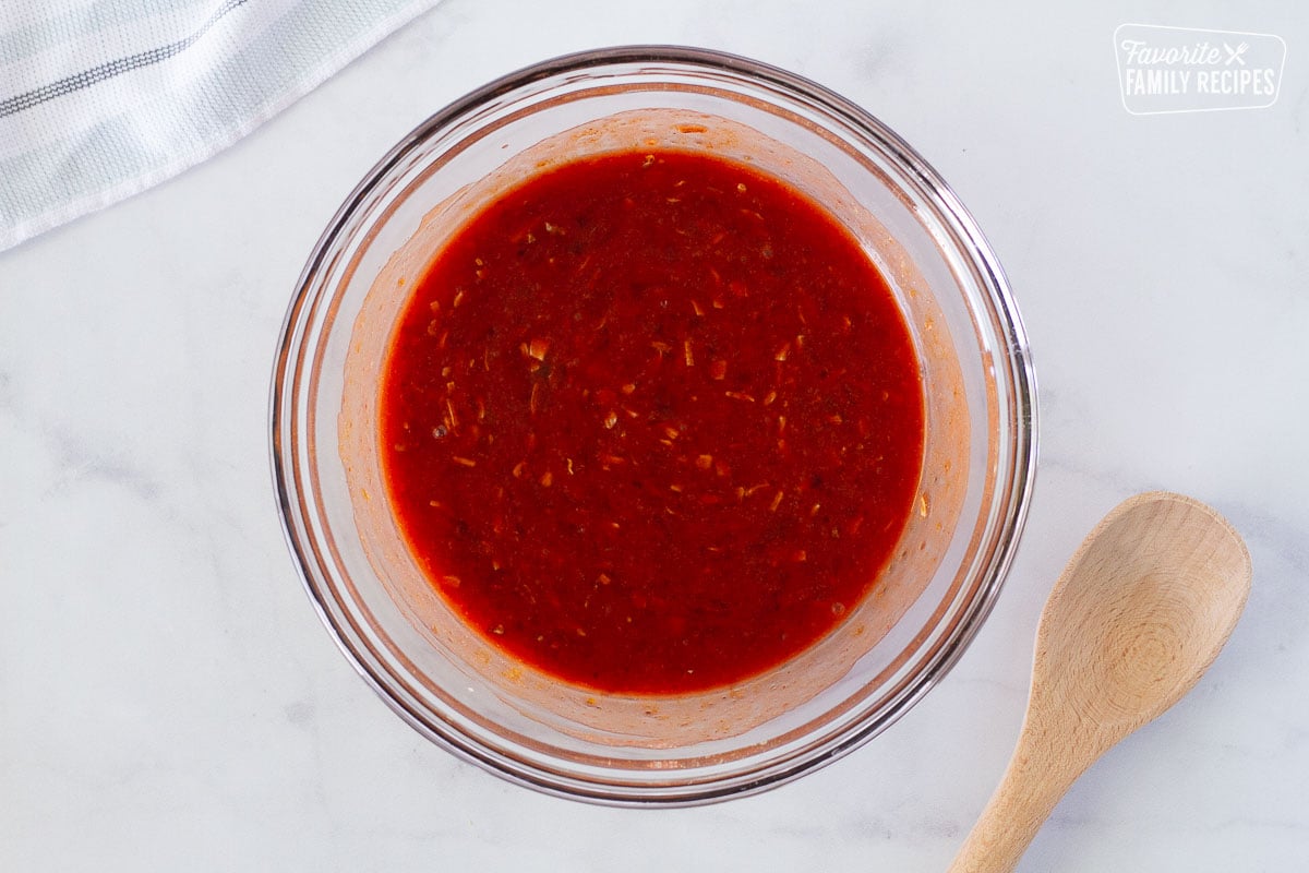 Bowl of sauce for Instant Pot Apricot Chicken. Wooden spoon on the side.