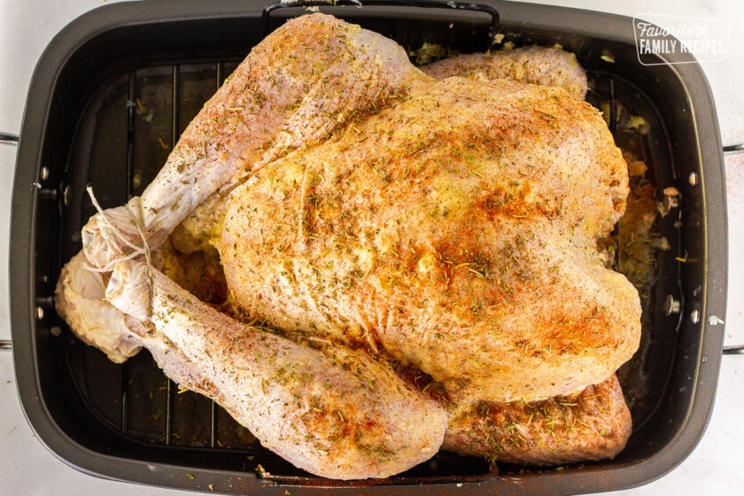 Seasoned uncooked turkey in a roasting pan for How to Cook a Turkey.