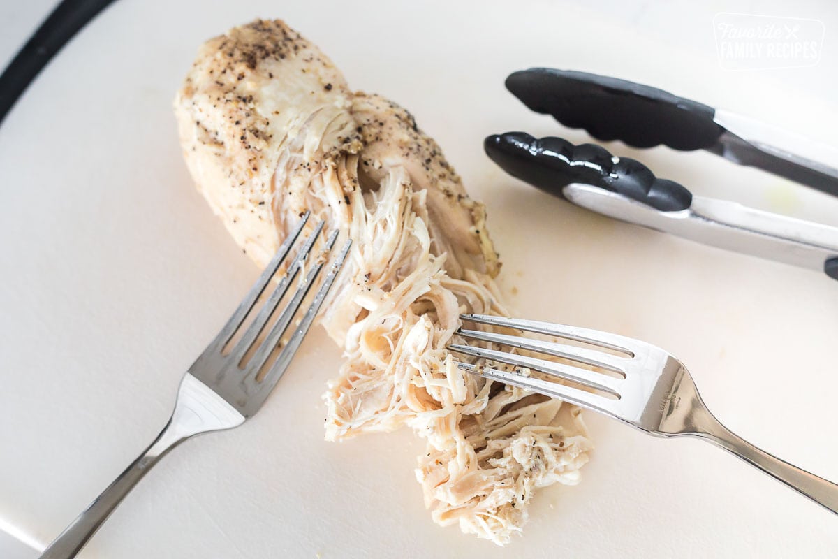 A cooked chicken breast being shredded with two forks