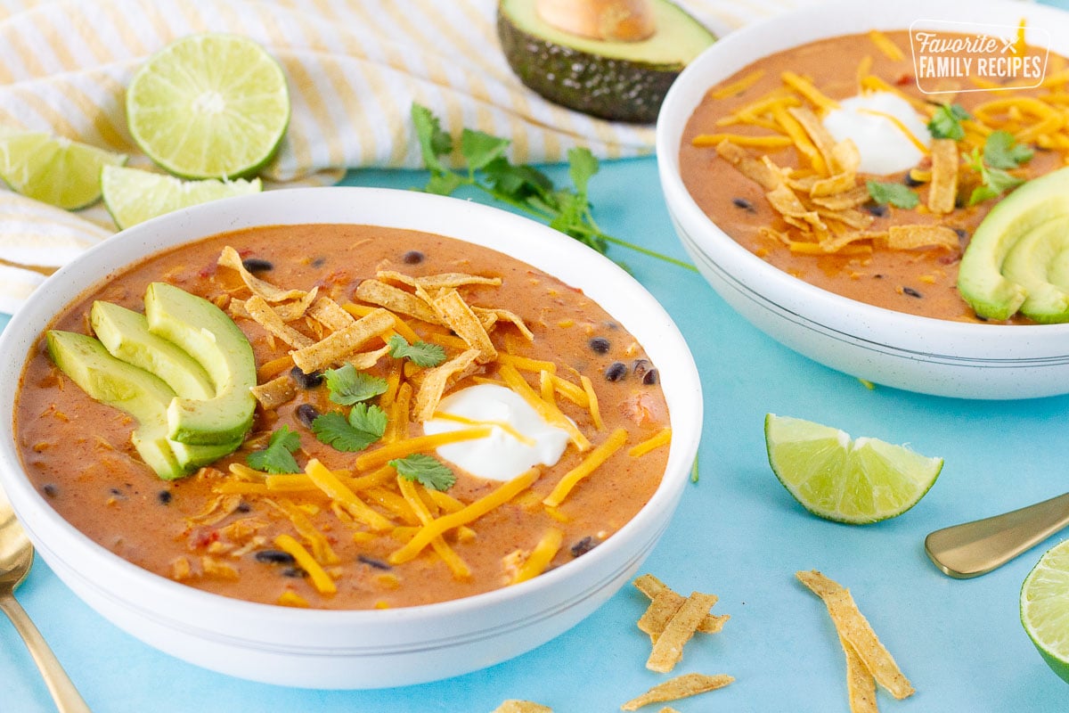 Side view of Cafe Zupas Chicken Enchilada Chili in bowls. Avocado, limes, tortilla strips, cheese and sour cream on top.