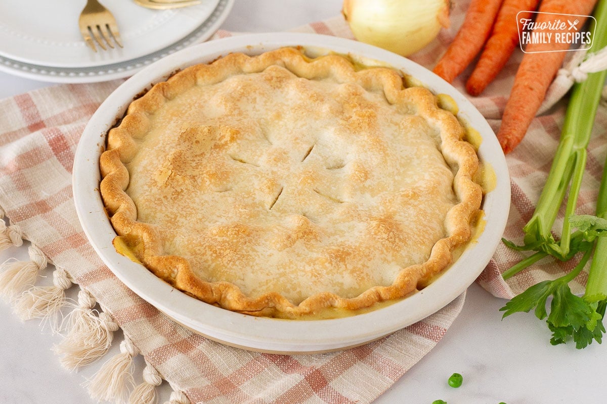 Side view of a whole Easy Turkey Pot Pie. Celery, carrots and onion on the side.