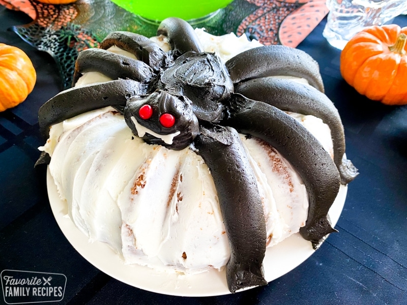 Spider bundt cake on a white plate with mini pumpkins around the plate.