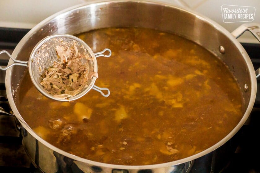 Mesh strainer full of pieces from turkey drippings in a pan for Turkey Gravy.