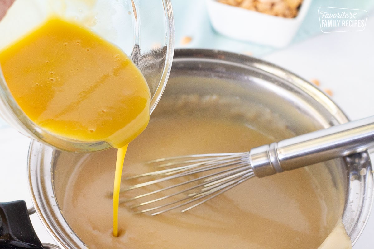 Adding tempered egg yolks into Butterscotch Pie filling with a whisk.