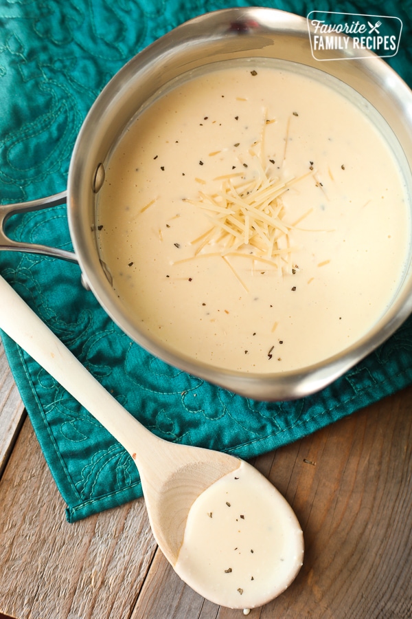 Homemade Alfredo sauce in a pan with shredded Parmesan on top.