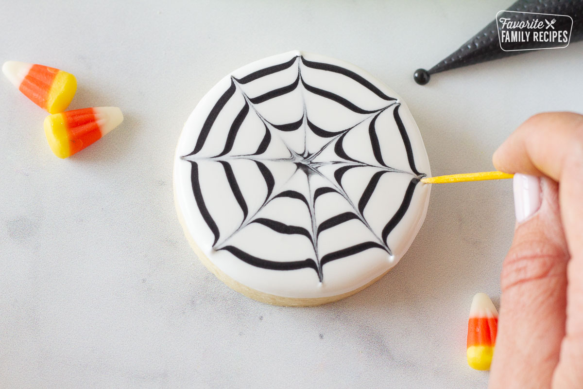 Hang holding toothpick moving the black icing for a spider web Halloween Cookie.