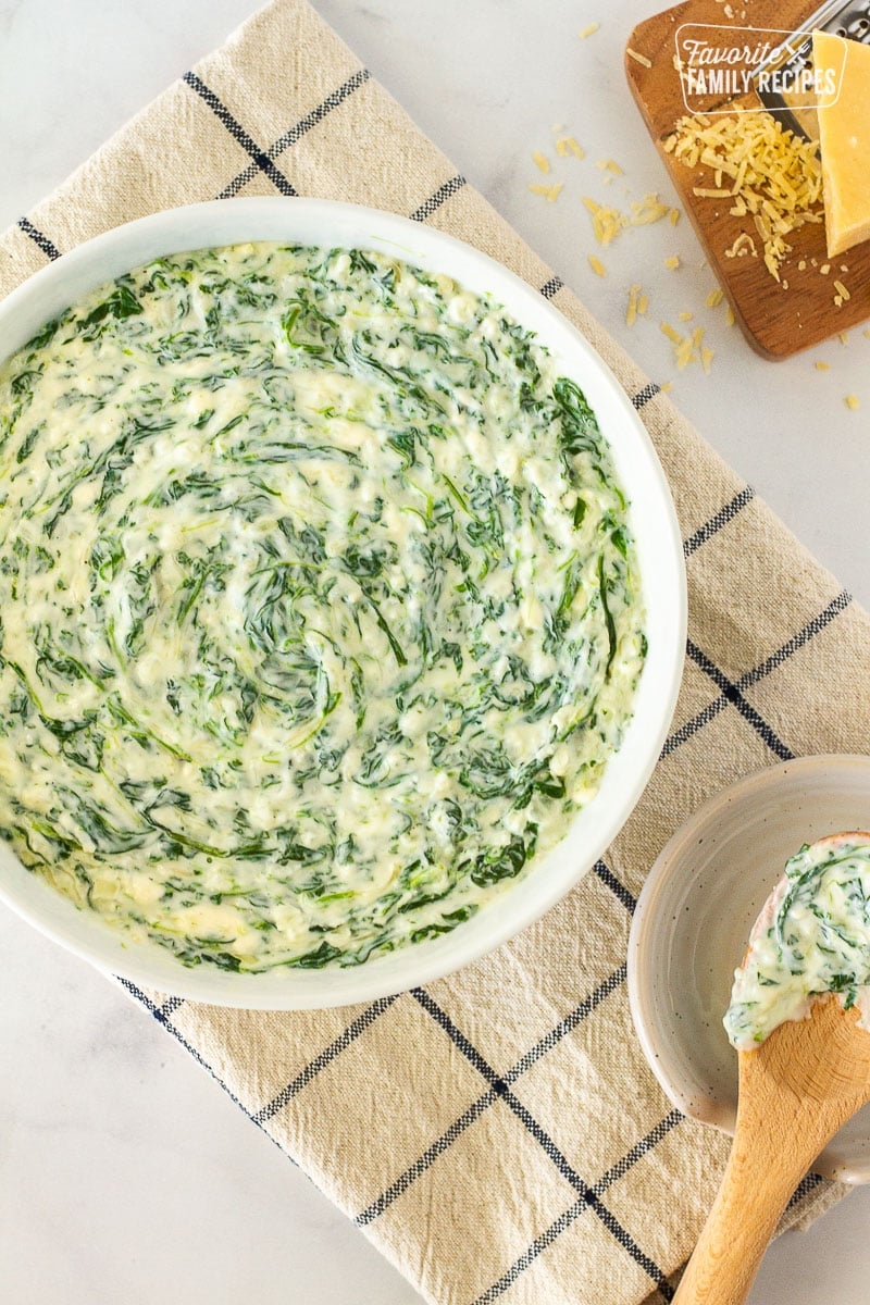 This is the best creamed spinach recipe you’ll ever taste! Three kinds of cheese and fresh spinach together with fragrant herbs and so easy to make! Top view of Creamed Spinach in a bowl next to a serving spoon in a saucer.