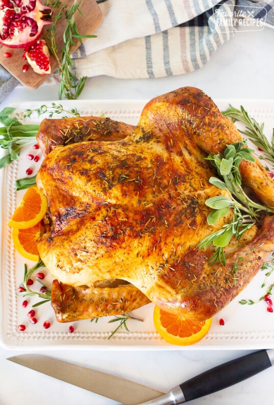 Turkey garnished with fresh pomegranate seeds, sage, rosemary, thyme and orange slices for How to Cook a Turkey.
