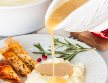 Turkey Gravy pouring on a plate of mashed potatoes and turkey.