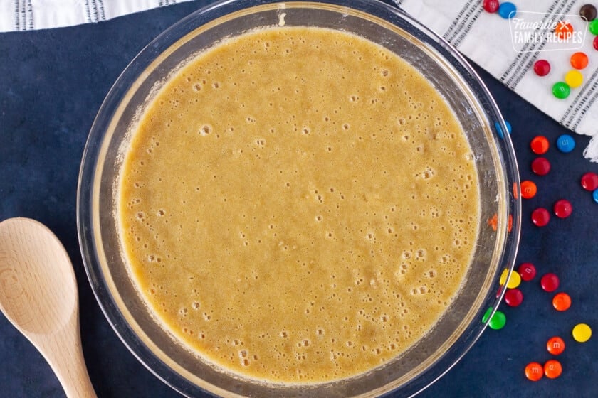 Wet ingredients combined in a large bowl for Monster Cookie Dough. Wooden spoon and M&Ms on the side.