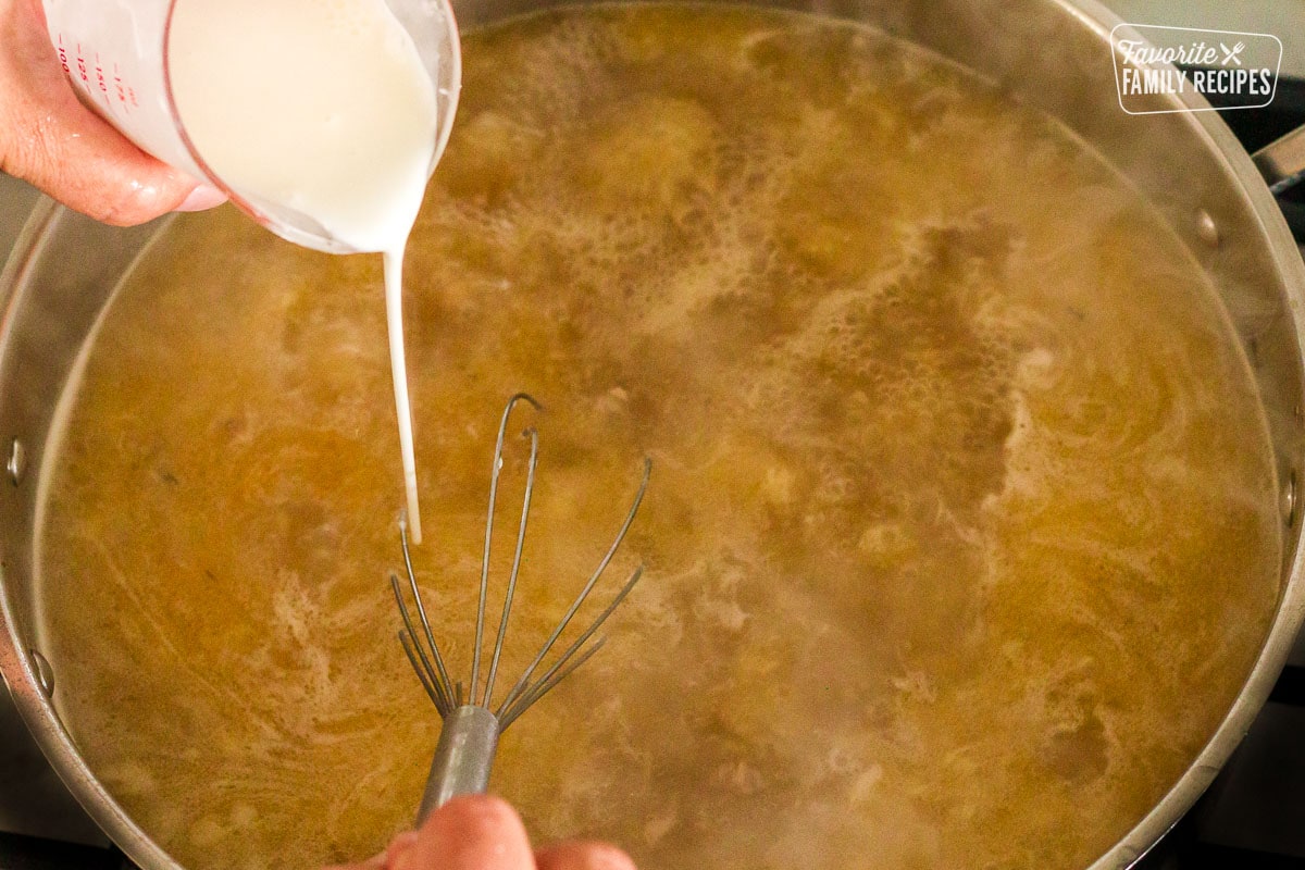 Whisking a pan of drippings while pouring slurry to thicken the Turkey Gravy.