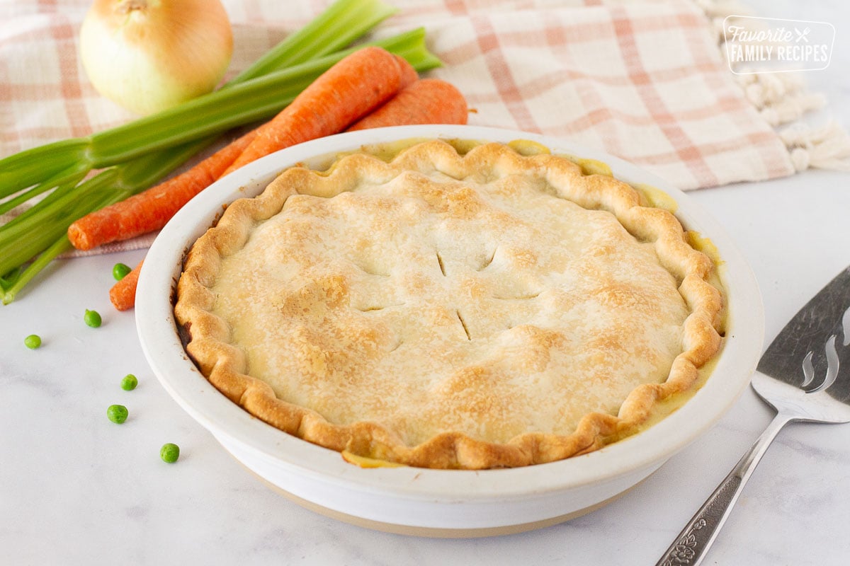 Whole Easy Turkey Pot Pie with a pie serving spatula. Carrots, celery, onion and peas on the side.